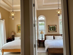 A bedroom with two beds, a chandelier, a window with a view, and a painting on the wall. - Luxury in Los Altos Hills Stanford Hospital and University. (Los Altos Hills)
