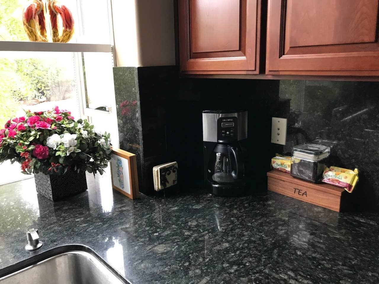 A kitchen with a coffee maker, a tea box, and a flower vase on the counter.