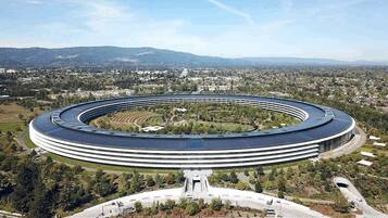 Un edificio grande y circular con un espacio abierto en el centro, rodeado de vegetación y un paisaje urbano al fondo.