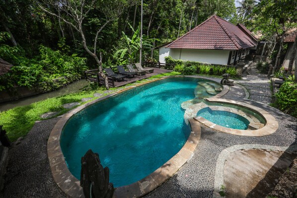A swimming pool with a curved design, surrounded by a stone deck and lush greenery.