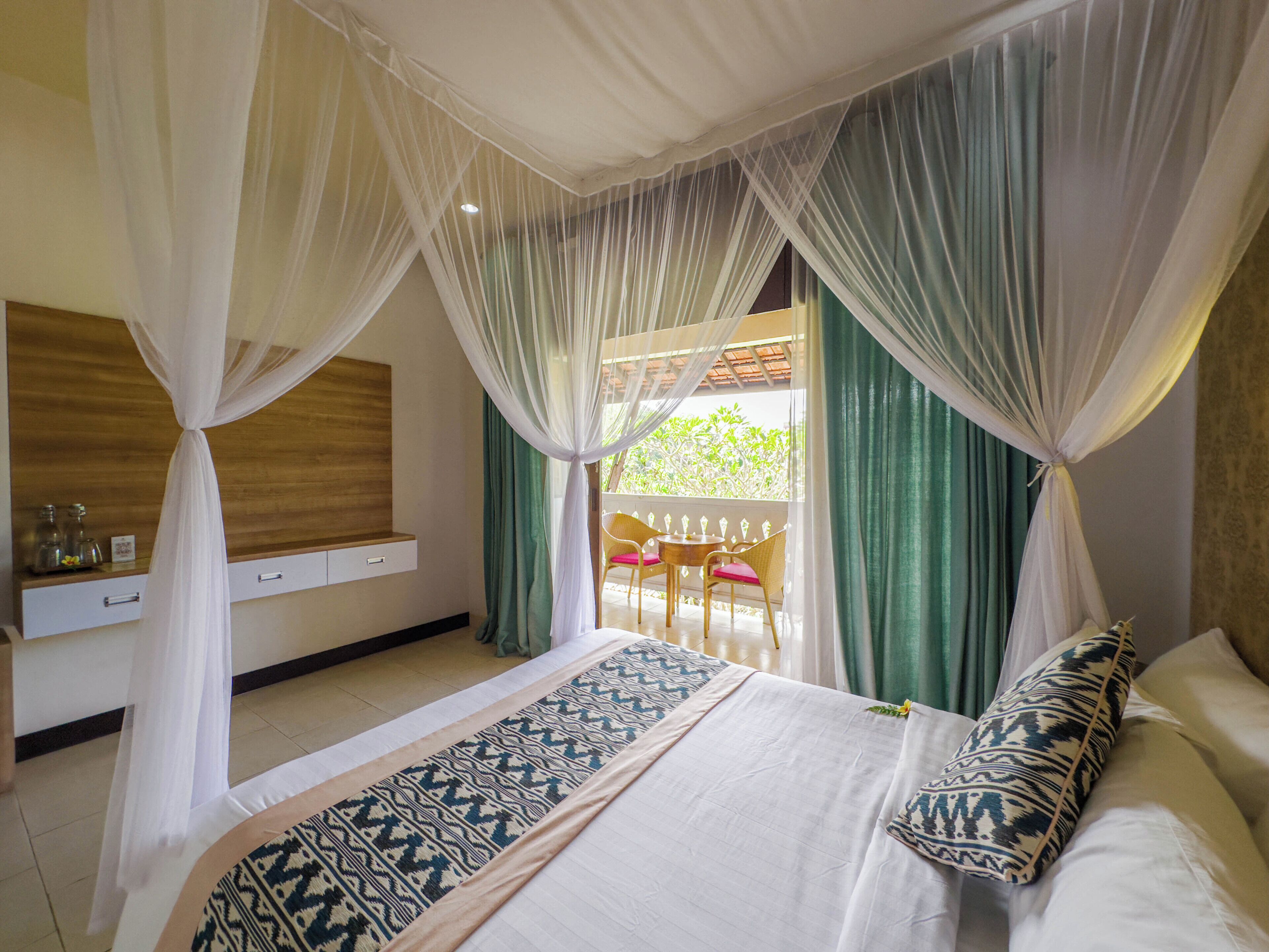 A bedroom with a bed, a nightstand, a window with curtains, and a view of the outdoors.