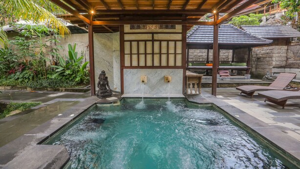 A tranquil outdoor pool area with a stone wall, a statue, and a covered seating area. - Ubud Sari Health Resort (Ubud)