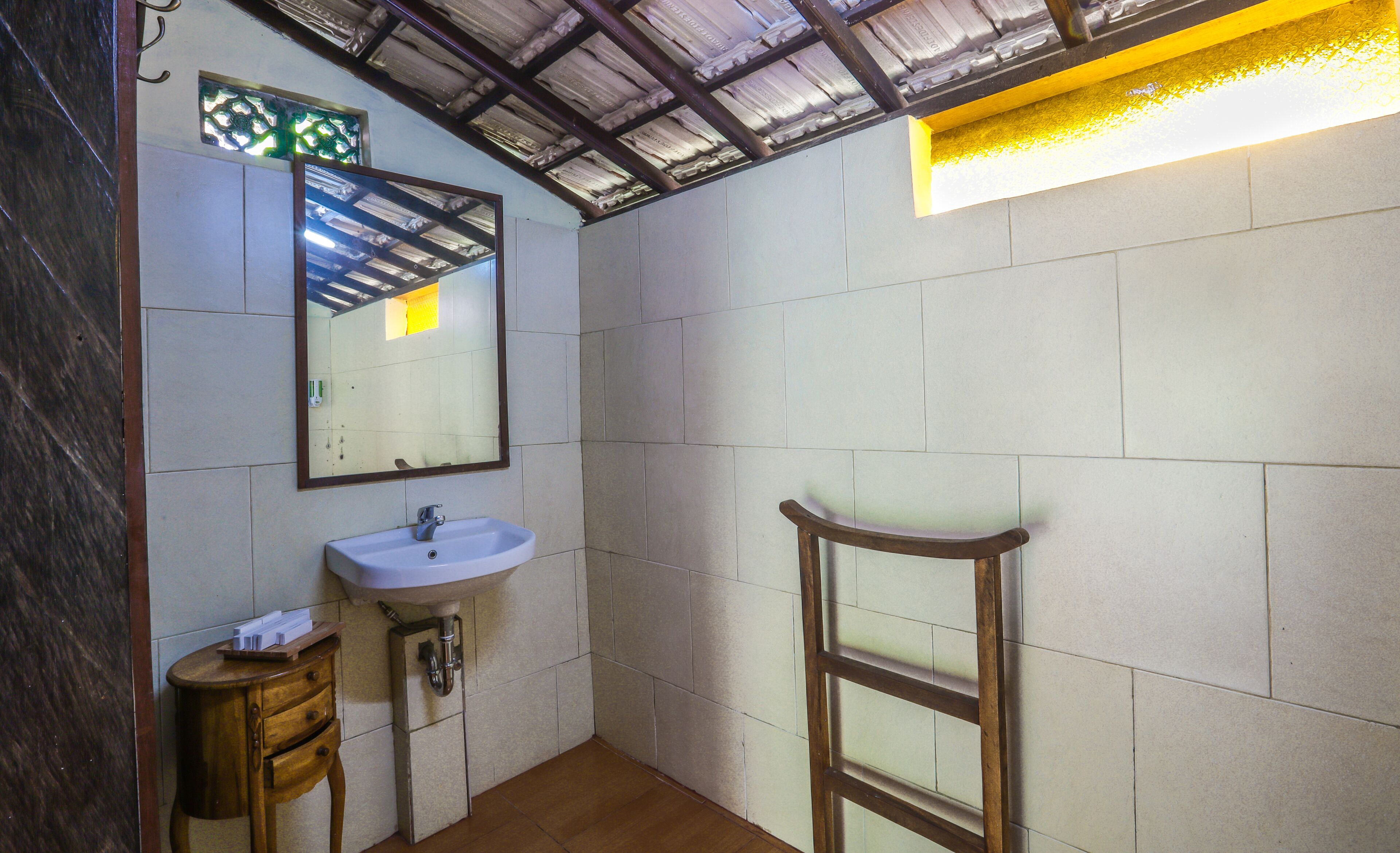 A bathroom with a sink, mirror, wooden chair, and tiled walls.