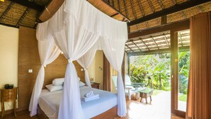 A bedroom with a four-poster bed, a bedside table, and a view of the garden through an open door. - Ubud Sari Health Resort (Ubud)