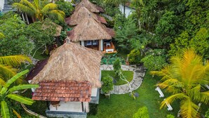 A tropical resort with thatched-roof cottages surrounded by lush greenery and palm trees. - Ubud Sari Health Resort (Ubud)