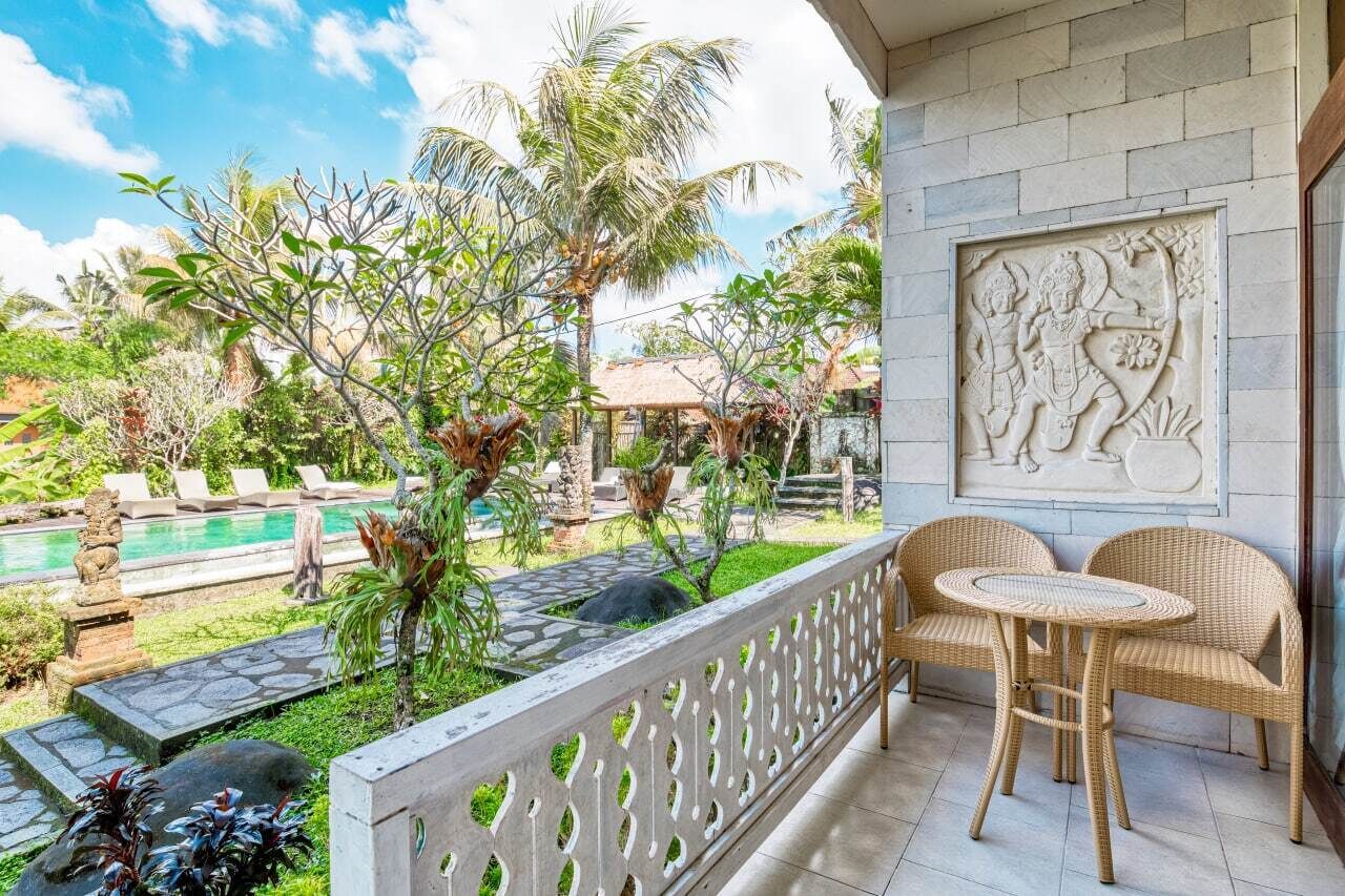 A balcony with wicker chairs, a decorative wall carving, a pool, and lush greenery.