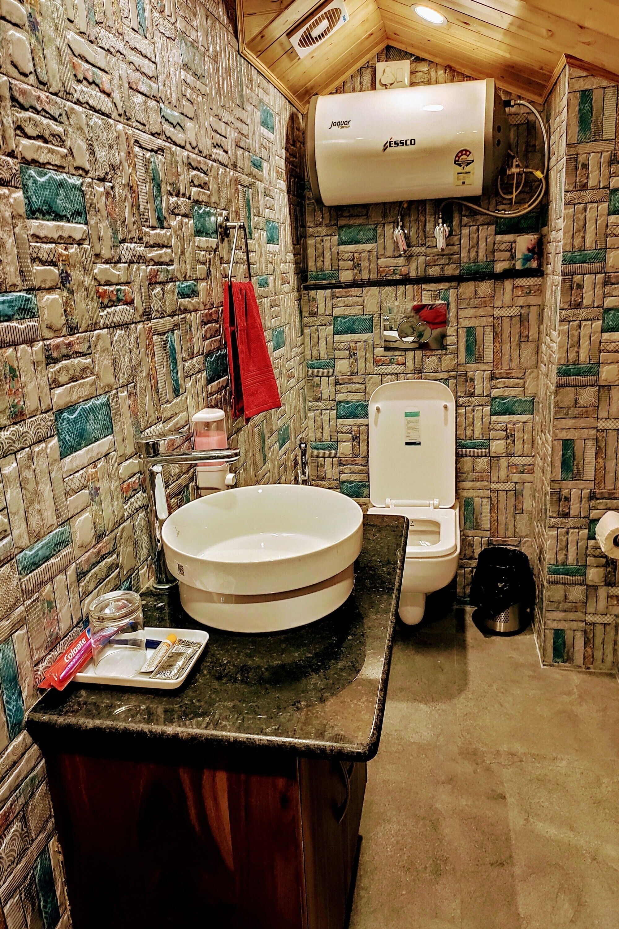 A bathroom with a stone mosaic wall, a white sink, a toilet, and a ceiling-mounted air conditioner.