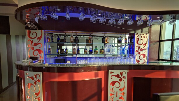 Un espace bar doté d’un comptoir incurvé, d’étagères remplies de bouteilles et de verres suspendus.
