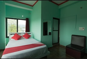Relax in a spacious room with a large bed, featuring a comfortable bedspread and pillows, and enjoy a view of lush greenery from the window.