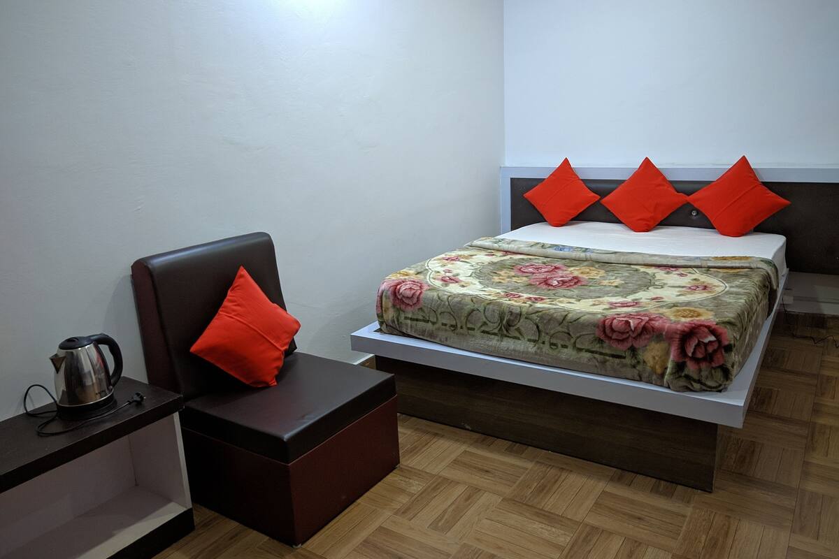 A bedroom with a bed, a chair, a nightstand, and a coffee maker.