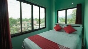 Une chambre d’hôtel avec un grand lit, deux oreillers rouges, une tête de lit blanche et une vue sur les immeubles à travers de grandes fenêtres.