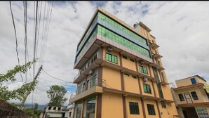 Un immeuble à plusieurs étages, doté d’une façade jaune, de grandes fenêtres et d’un balcon au deuxième étage.