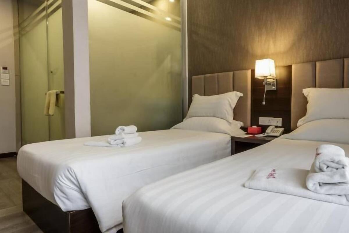 A hotel room with two beds, each with a pillow and a rolled towel.