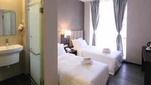 Une chambre d’hôtel avec une salle de bain, deux lits, une table de chevet, une lampe et une fenêtre avec des rideaux.