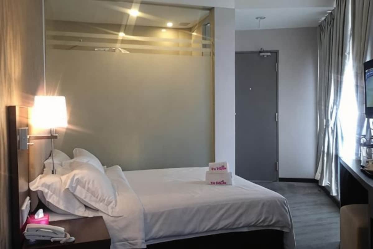Ett hotellrum med en säng, ett nattduksbord, en lampa och en dörr.