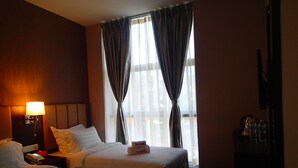 Une chambre d’hôtel avec deux lits, une table de chevet avec une lampe, un téléphone et une fenêtre avec des rideaux.
