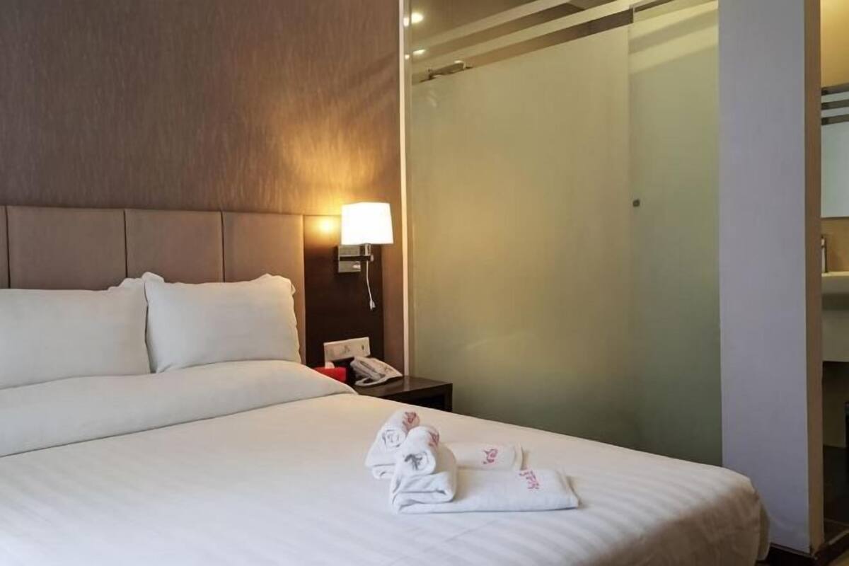 A hotel room with a large bed, a bedside lamp, a glass shower enclosure, and a telephone on the nightstand.