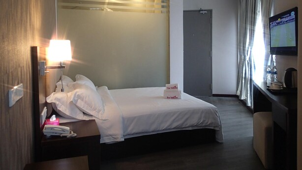 Une chambre d’hôtel équipée d’un lit, d’une table de chevet, d’une lampe, d’une télévision et donnant sur le couloir.