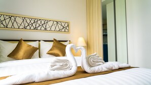 A neatly made bed with white and gold pillows, a heart-shaped towel arrangement, and a wall art piece above the bed. - Azalea Suites Cikarang by Jayakarta Grup (Cikarang)