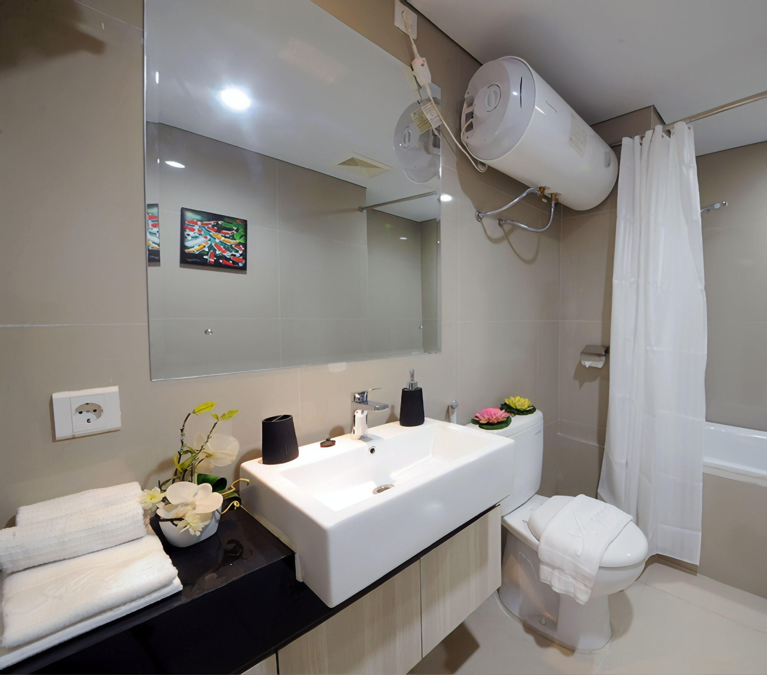 A modern bathroom with a white sink, mirror, and toilet. There is a hairdryer mounted on the wall, a towel rack, and a small plant on the counter.