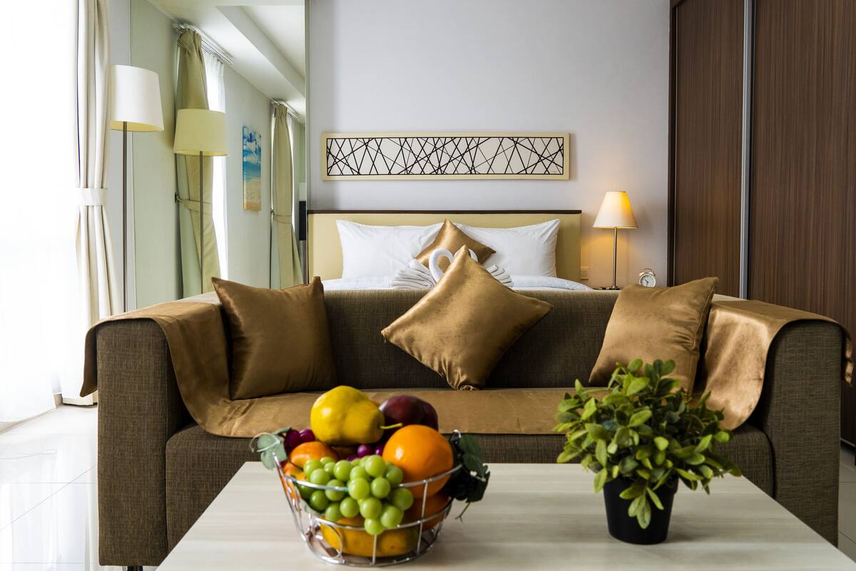 A modern hotel room with a sofa, pillows, a fruit bowl, and a potted plant.