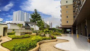 A courtyard with a landscaped garden, a modern building with balconies, and a high-rise building in the background. - Azalea Suites Cikarang by Jayakarta Grup (Cikarang)