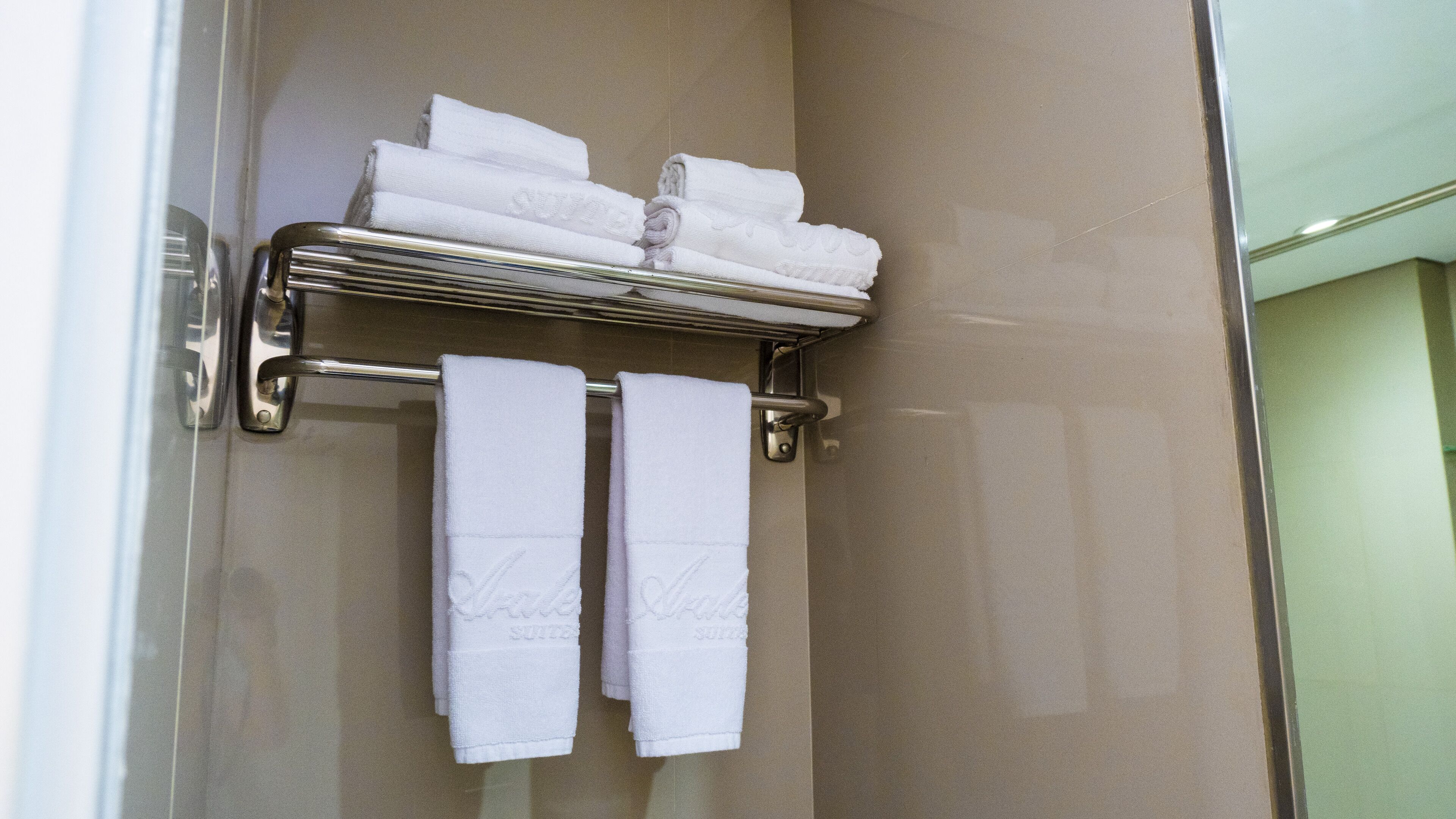 A bathroom with a glass shower door, a towel rack with folded towels, and a towel rack with two towels hanging.