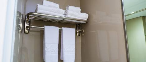 A bathroom with a glass shower door, a towel rack with folded towels, and a towel rack with two towels hanging.