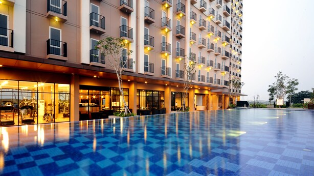 A hotel with a large outdoor swimming pool, multiple balconies, and well-lit windows. - Azalea Suites Cikarang by Jayakarta Grup (Cikarang)