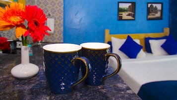 Une pièce avec un lit, deux tasses bleues posées sur un comptoir et un vase contenant des fleurs oranges.