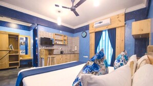 A bedroom with a bed, a ceiling fan, a built-in TV, a small kitchenette, and a bathroom with a shower. - Habitat by Liwa (Bengaluru)