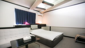 A hotel room with a white sofa, a single bed, a small table with a tissue box, a bedside lamp, and a window with a curtain. - Kanku Kokusai Hotel (Wakayama)