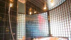 A modern bathroom with a red-tiled floor, a large bathtub, and a shower area. - Kanku Kokusai Hotel (Wakayama)