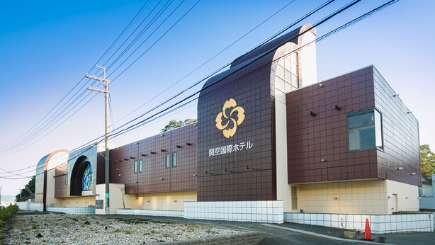 A modern building with a distinctive logo, a large arched entrance, and a tiled facade. - Kanku Kokusai Hotel (Wakayama)