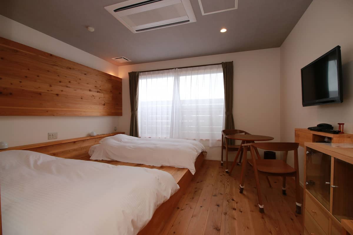Une chambre d’hôtel avec deux lits, un plafond en bois, une télévision, un bureau et une fenêtre avec des rideaux.