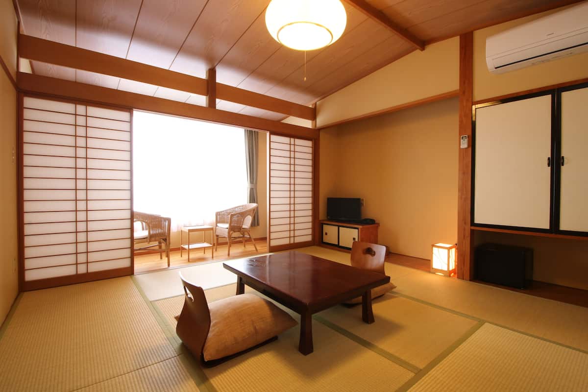 Une pièce de style japonais traditionnel, avec un sol recouvert de tatamis, une basse table en bois, un banc rembourré, des portes coulissantes, un téléviseur et un meuble.