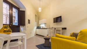 Un espacio habitable compacto con comedor, kitchenette y un sofá amarillo.
