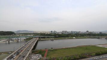 A highway overpass with multiple lanes of traffic, a river below, and a cityscape in the background.
