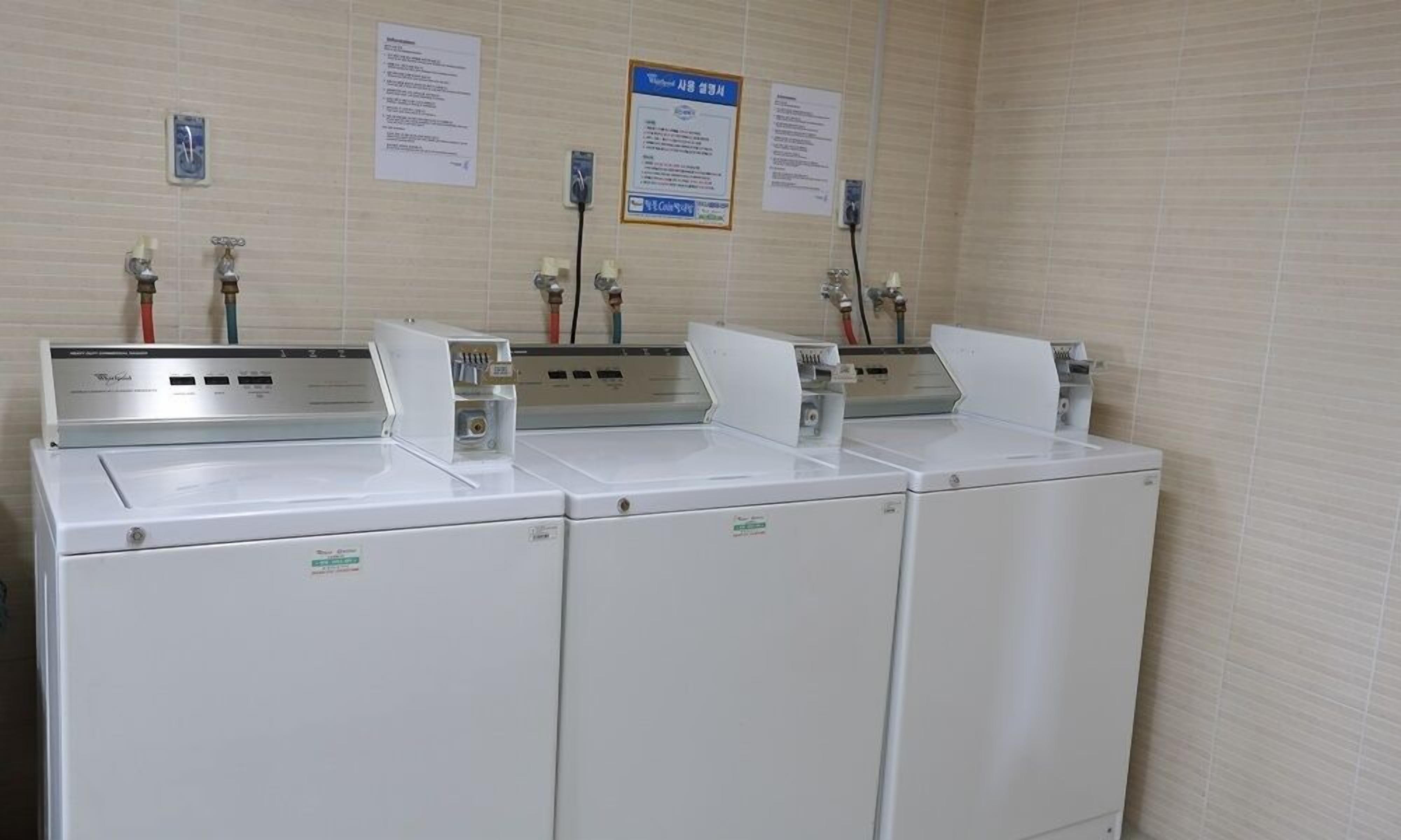 Una sala de lavandería con tres lavadoras blancas y dos dispensadores de agua.