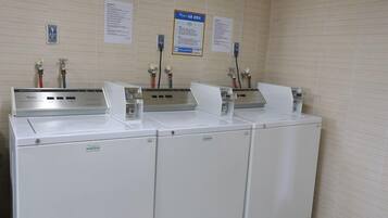 Una sala de lavandería con tres lavadoras blancas y dos dispensadores de agua.