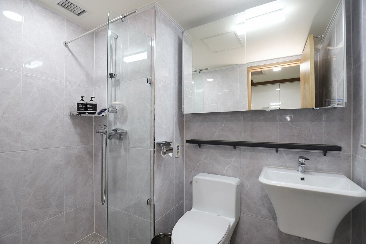Un baño moderno con cabina de ducha de vidrio, inodoro blanco y lavamanos sobre pedestal.
