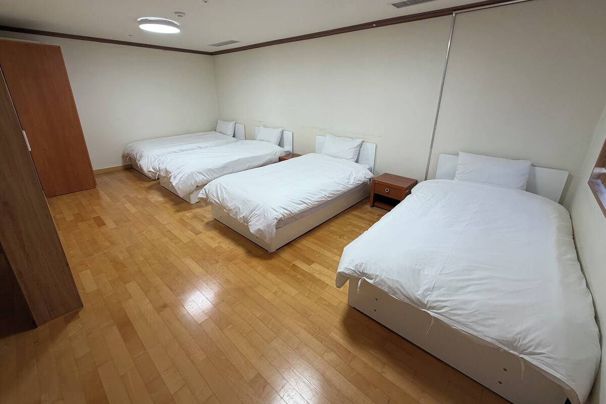 A hotel room with three single beds, wooden flooring, and a wooden wardrobe.
