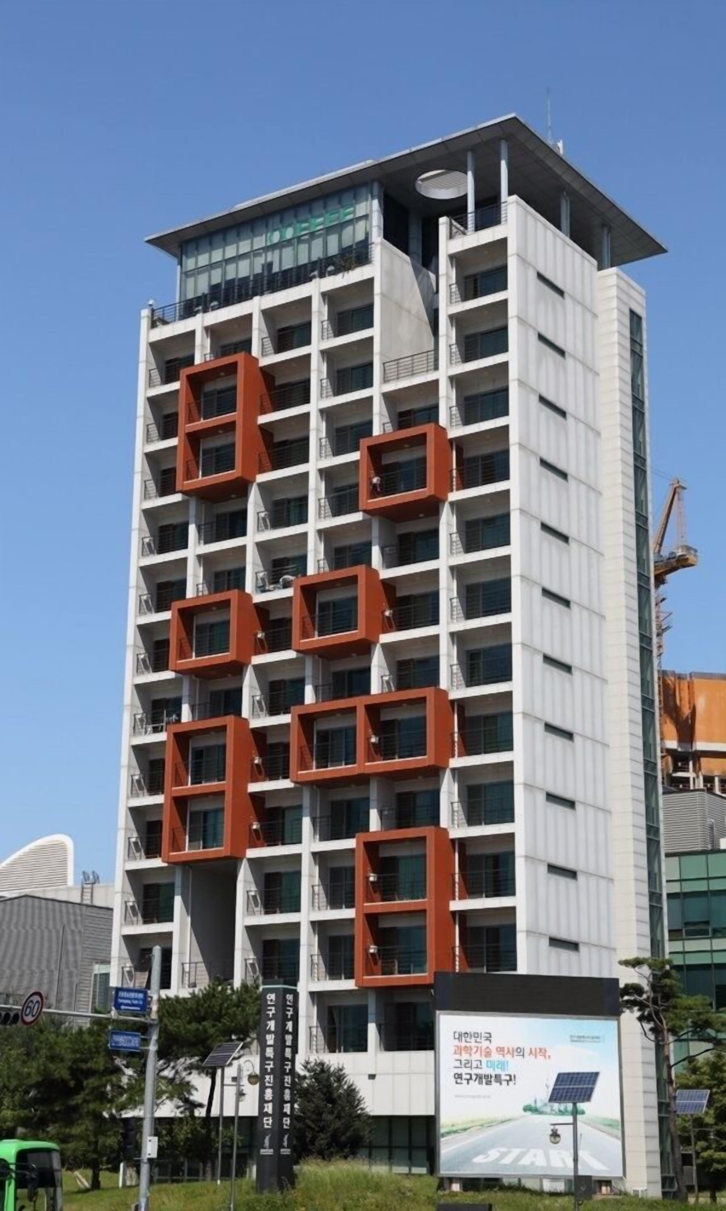 A modern building with a unique architectural design, featuring multiple balconies and a prominent rooftop structure.