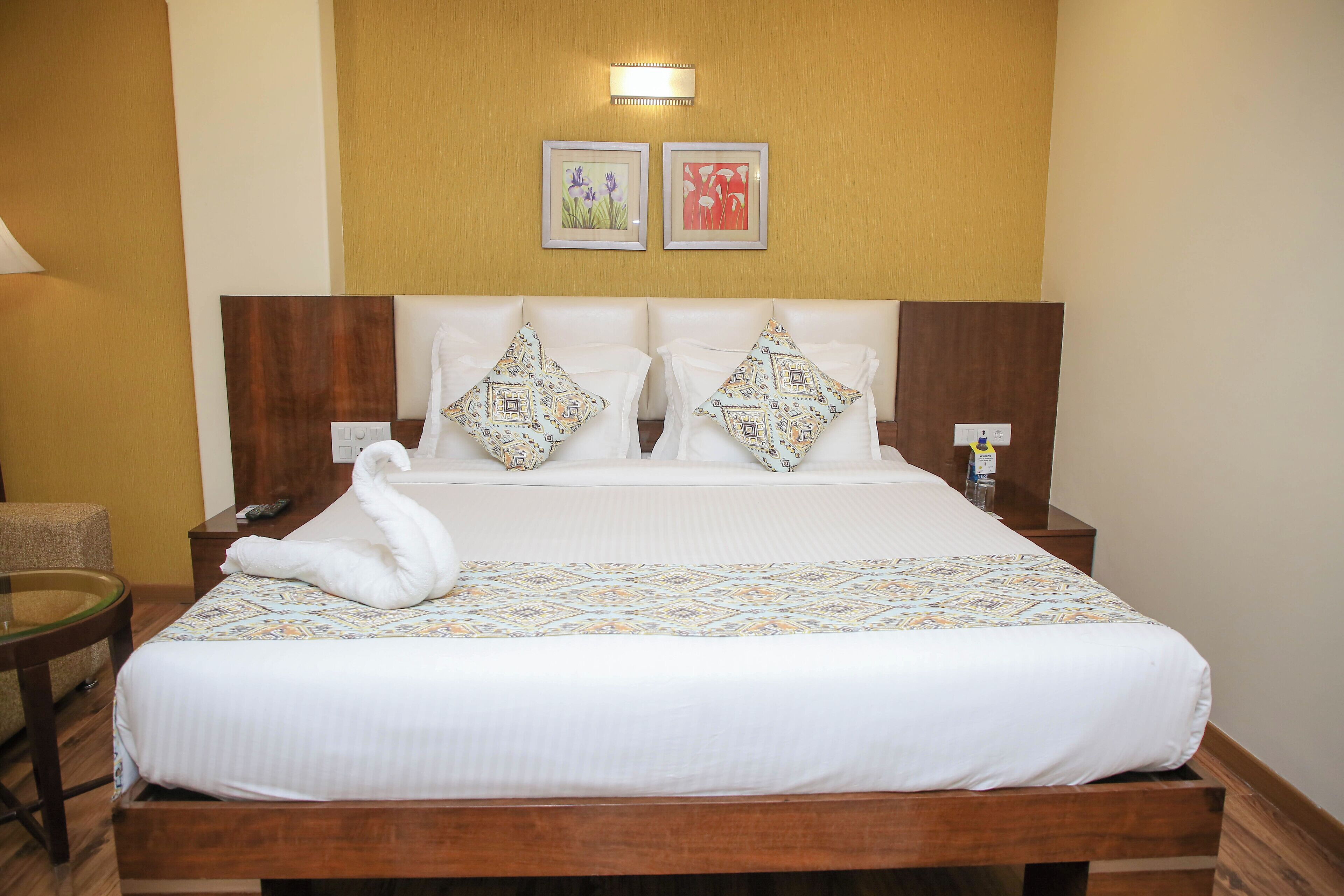 Una cama bien hecha con almohadas estampadas, una mesita de noche con lámpara y dos cuadros en la pared.