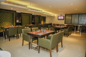 A restaurant with multiple tables and chairs, a television screen, and a modern interior design. - Hotel Citrus Prime (Raipur)