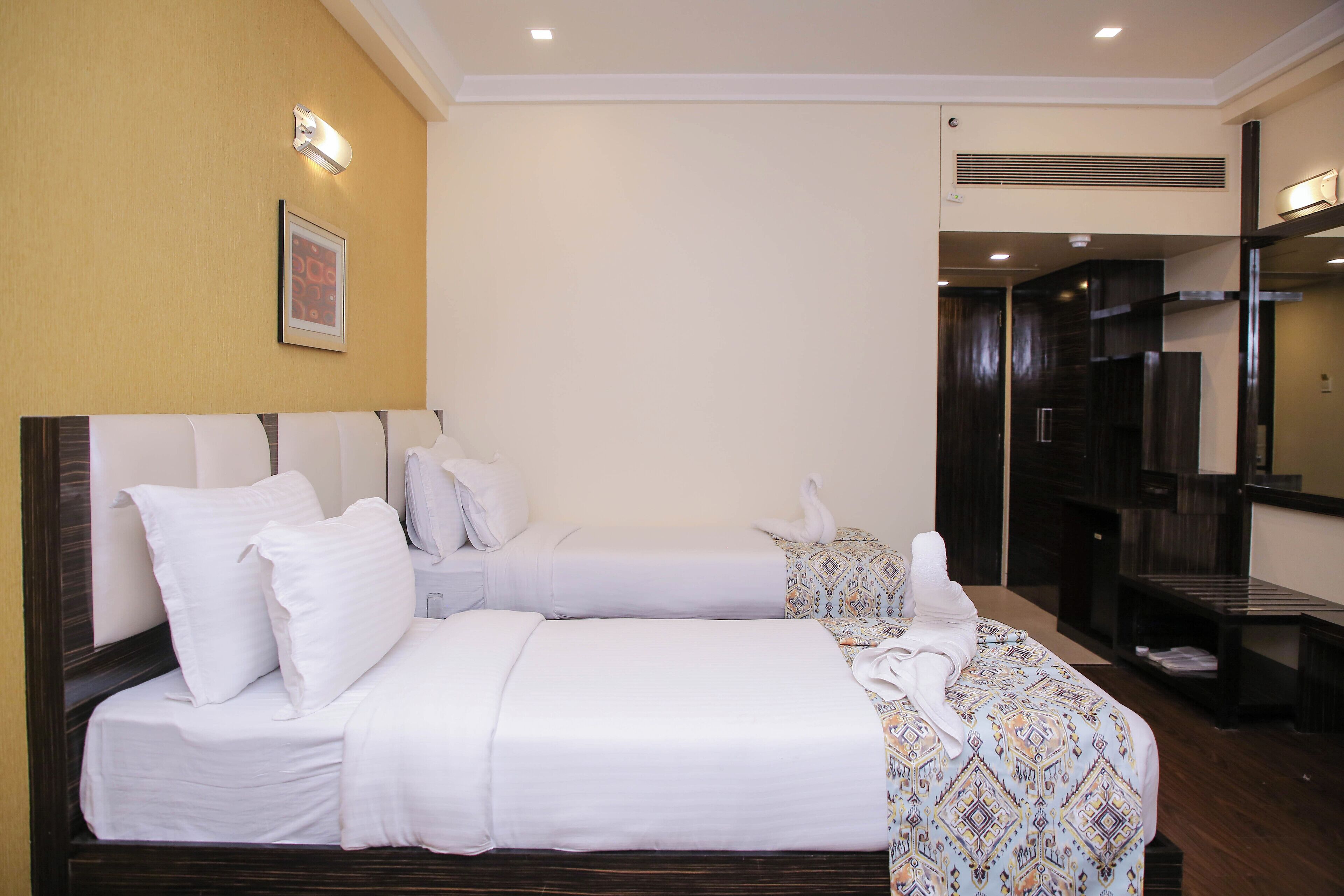 A hotel room with two beds, a wooden headboard, a framed picture on the wall, and a dark wooden wardrobe.