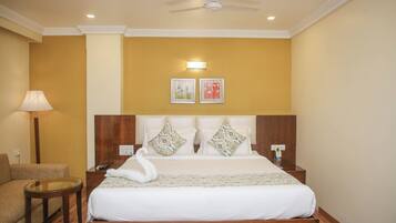 A hotel room with a bed, a chair, a lamp, and two wall-mounted pictures.