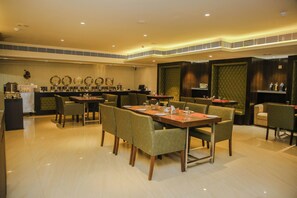 A restaurant with multiple dining tables and chairs, a bar area with a counter and stools, and a buffet setup with food items. - Hotel Citrus Prime (Raipur)