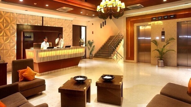 A hotel lobby with a reception desk, two receptionists, a staircase, and an elevator. - Hotel Citrus Prime (Raipur)