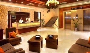 A hotel lobby with a reception desk, two receptionists, a staircase, and an elevator. - Hotel Citrus Prime (Raipur)
